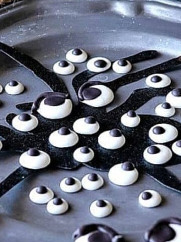 A pewter plate filled with Homemade Candy Eyeballs and a spider silhouette.