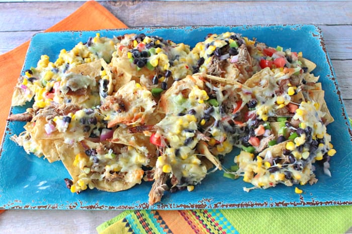 A colorful photo of Loaded Pulled Pork Nachos on an aqua blue tray with a lime green and orange napkin underneath.