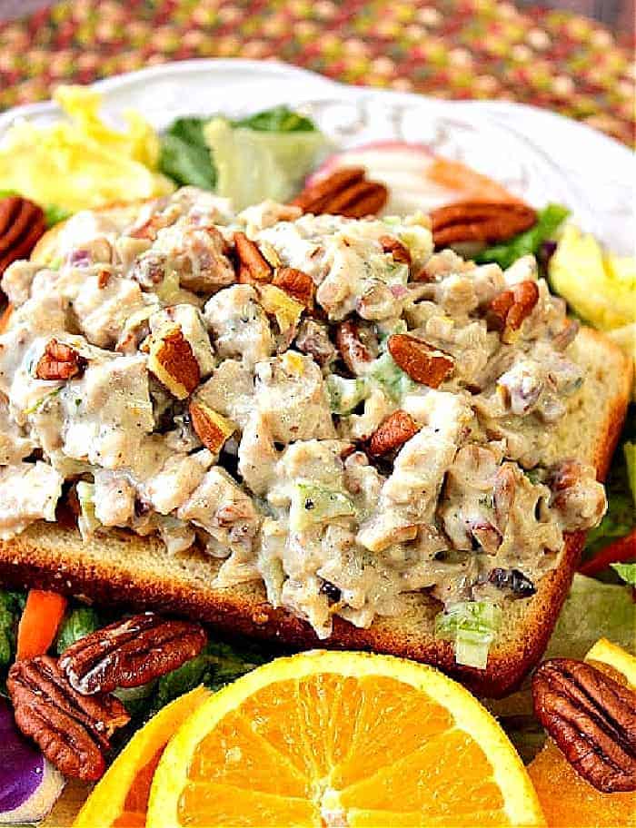 A closeup vertical image of a colorful orange cashew chicken salad with pecans on a white plate.