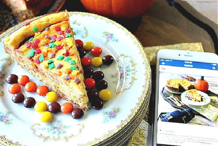 A slice of Reese's Pieces Pumpkin Cheesecake on a pretty plate with fall sprinkles and an iphone with a photo.