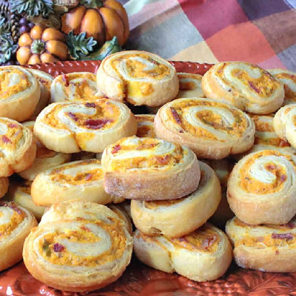 A stack of Pumpkin Crescent Pinwheel Appetizers on an orange platter.