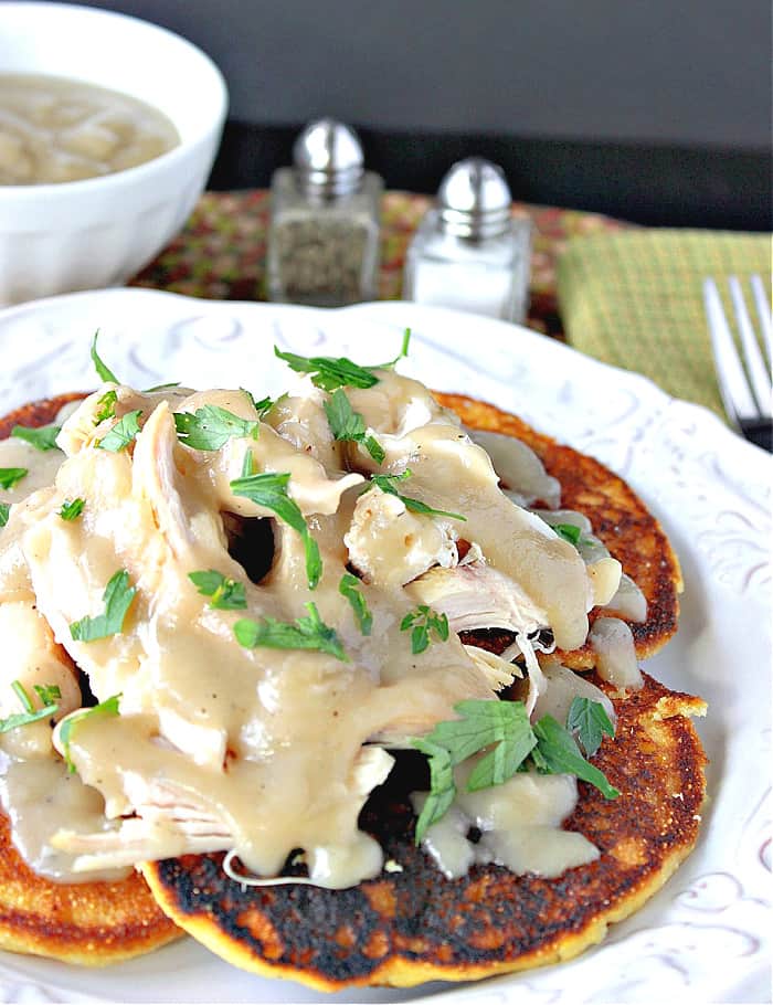 A closeup vertical image of Chicken Chile Corn Cakes topped with maple gravy and fresh parsley.