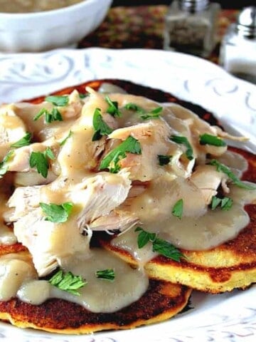 A pretty white plate filled with Chicken Chile Corn Cakes and covered with Buttery Maple Gravy and parsley as garnish