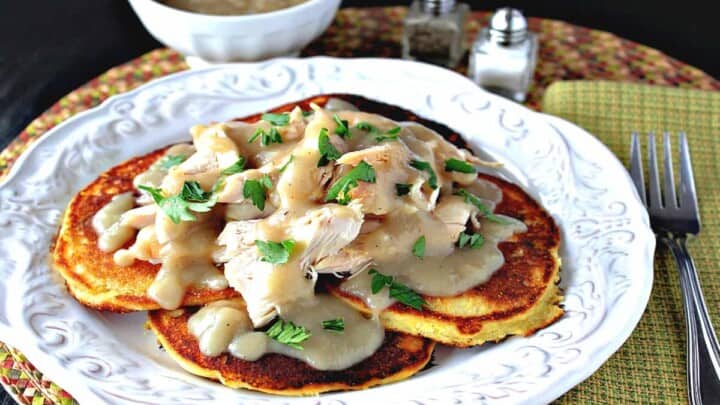 A pretty white plate filled with Chicken Chile Corn Cakes and covered with Buttery Maple Gravy and parsley as garnish