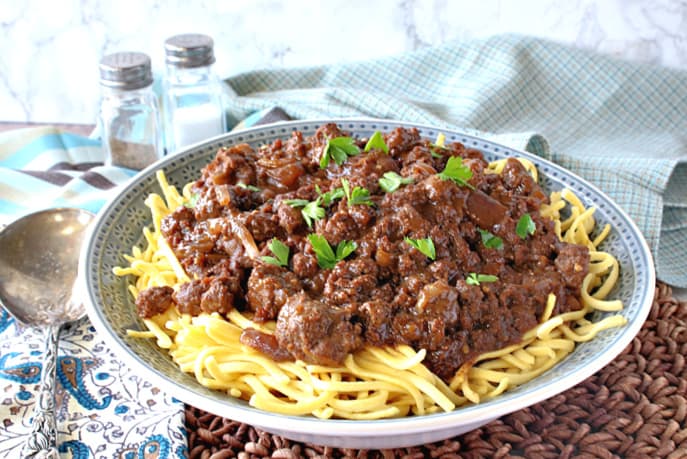 A blue bowl filled with ground beef sauerbraten goulash along with a serving spoon and some blue napkins.