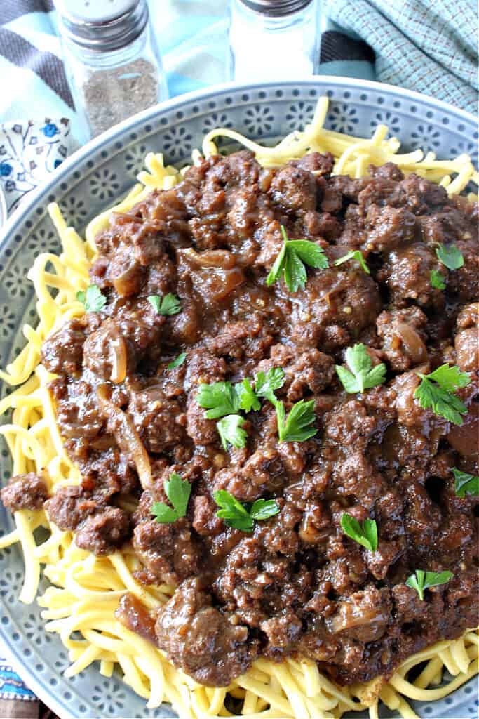 An overhead vertical closeup of a blue bowl filled with ground beef sauerbraten goulash served over noodles