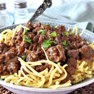 A blue bowl filled with ground beef sauerbraten goulash along with a serving spoon and parsley