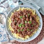 A round blue plate filled with Ground Beef Sauerbraten Goulash over noodles.