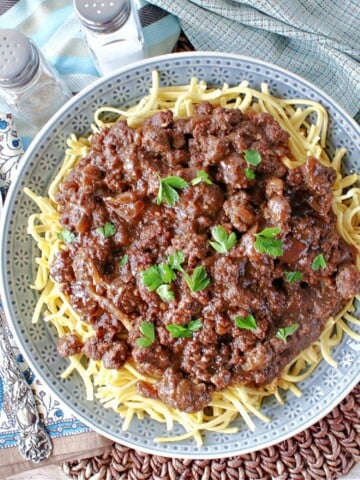 A round blue plate filled with Ground Beef Sauerbraten Goulash over noodles.
