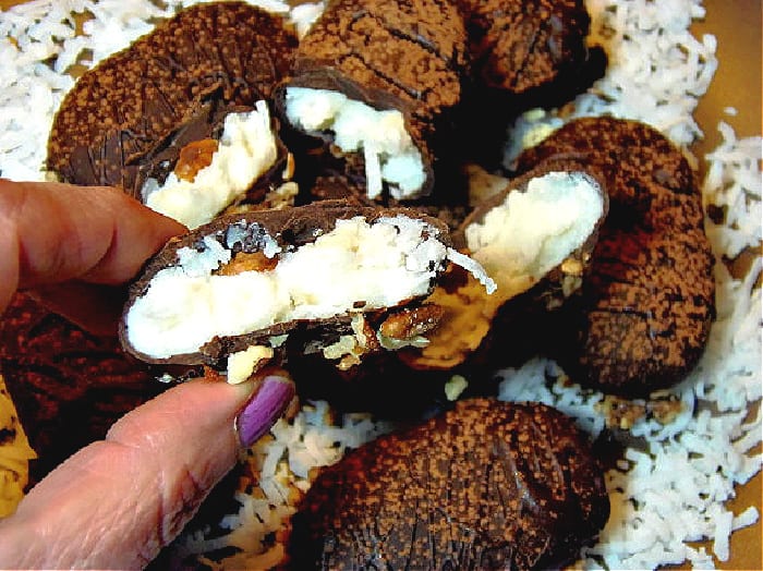 A closeup photo of a hand holding a piece of Homemade Almond Joy Candy with a bite taken out.