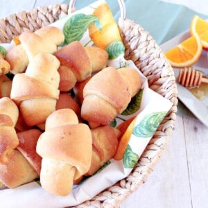 A basket filled with golden Homemade Crescent Rolls with honey and orange.