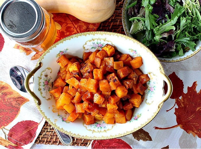 Directly overhead photo of a pretty china bowl with gold handles filled with bright orange honey roasted butternut squash.