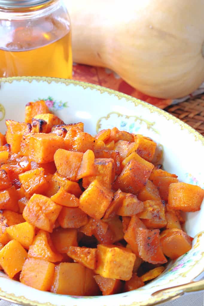 A closeup vertical image of beautiful orange honey roasted butternut squash in a pretty china bowl with gold trim