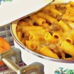A casserole dish filled with pumpkin cream pasta with bratwurst and a small pumpkin on the side.