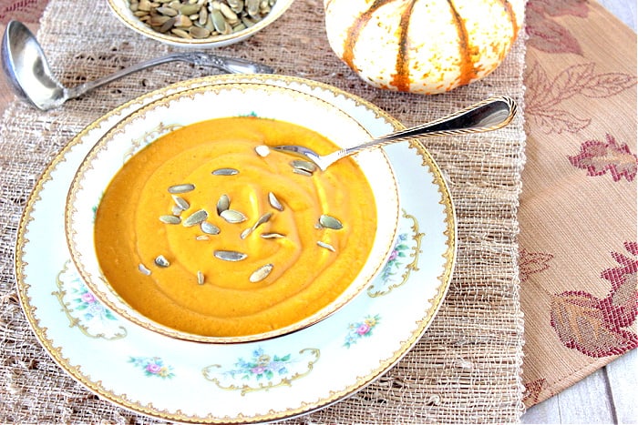 An offset photo of a bowl of Roasted Butternut Squash Soup on a textured placemat with a leaf napkin.