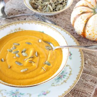 An offset overhead photo of a pretty bowl filled with roasted butternut squash and vegetable soup with a spoon and pepita seeds on top.
