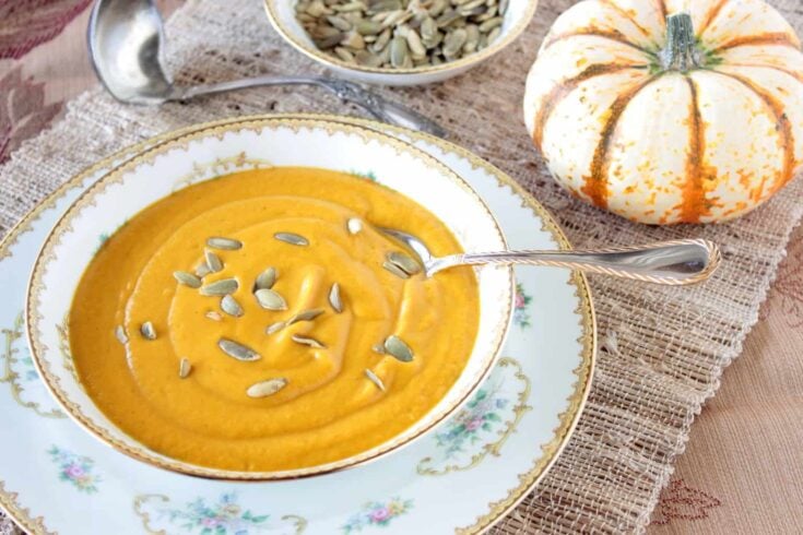 An offset overhead photo of a pretty bowl filled with roasted butternut squash and vegetable soup with a spoon and pepita seeds on top.