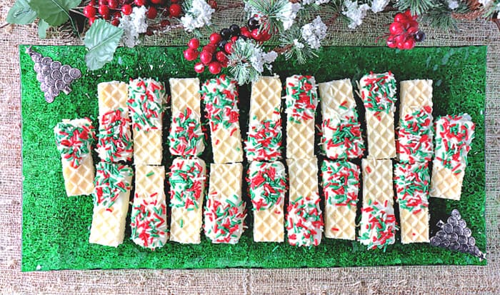 A direct overhead photo of a green glass rectangle plate filled with No-Bake Peppermint Buttercream Wafer Cookies with snow covered greens and berries in the background.