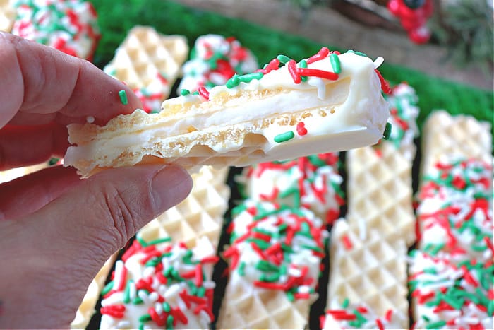 A closeup size view photo of a No-Bake Peppermint Buttercream Wafer Cookie dipped in white chocolate and Christmas sprinkles 