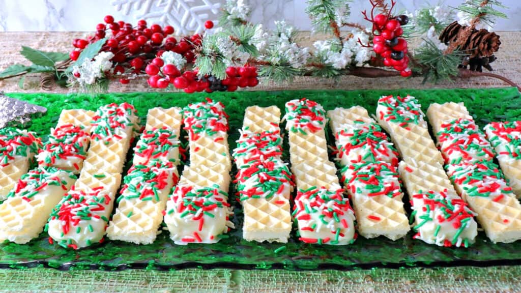 A bunch of Peppermint Buttercream Wafer Cookies on a green glass plate with holiday sprinkles.