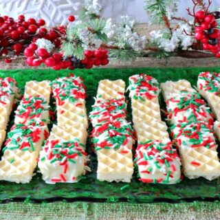 A bunch of Peppermint Buttercream Wafer Cookies on a green glass plate with holiday sprinkles.