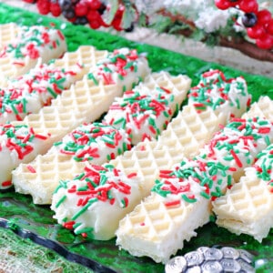 A bunch of Peppermint Buttercream Wafer Cookies on a green glass plate with holiday sprinkles.