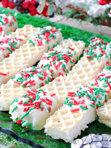 A bunch of Peppermint Buttercream Wafer Cookies on a green glass plate with holiday sprinkles.