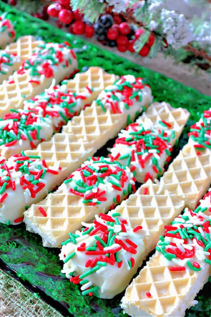 Vertical closeup photo of a tray of No-Bake Peppermint Buttercream Wafer Cookies with greens and berries in the background.