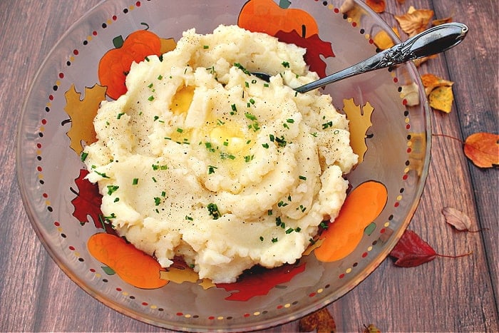 An overhead photo of a colorful bowl filled with Celery Root Mashed Potatoes along with a spoon and autumn leaves.