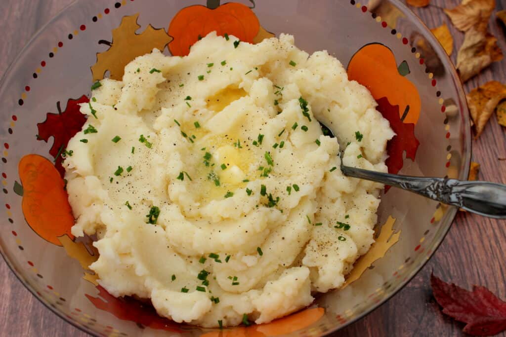 A bowl full of Celery Root Mashed Potatoes along with melting butter.