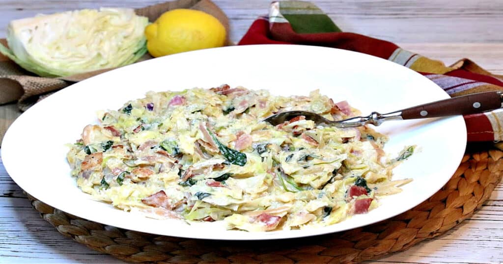 An oblong white bowl filled with Creamed Cabbage and Spinach with a serving spoon in the center.