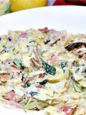 Creamed Cabbage with Spinach and Bacon in a white bowl with a lemon in the background.