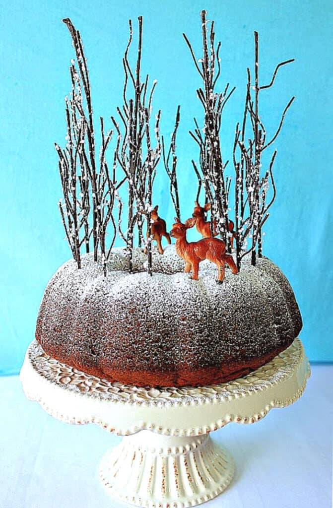 A Gingerbread Forest Cake with confectioners sugar dusting and tall trees with deer.