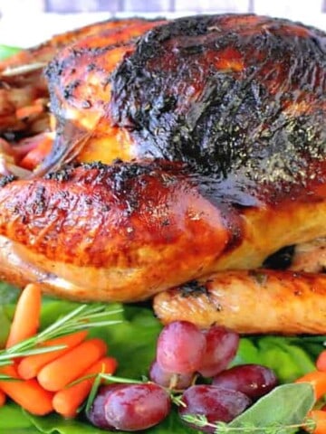 A beautifully browned roasted turkey on a platter with grapes, carrots, and greens.