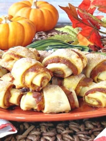 A bunch of Pumpkin Pie Bites on a small pumpkin plate with real mini pumpkins in the background and fall leaves.