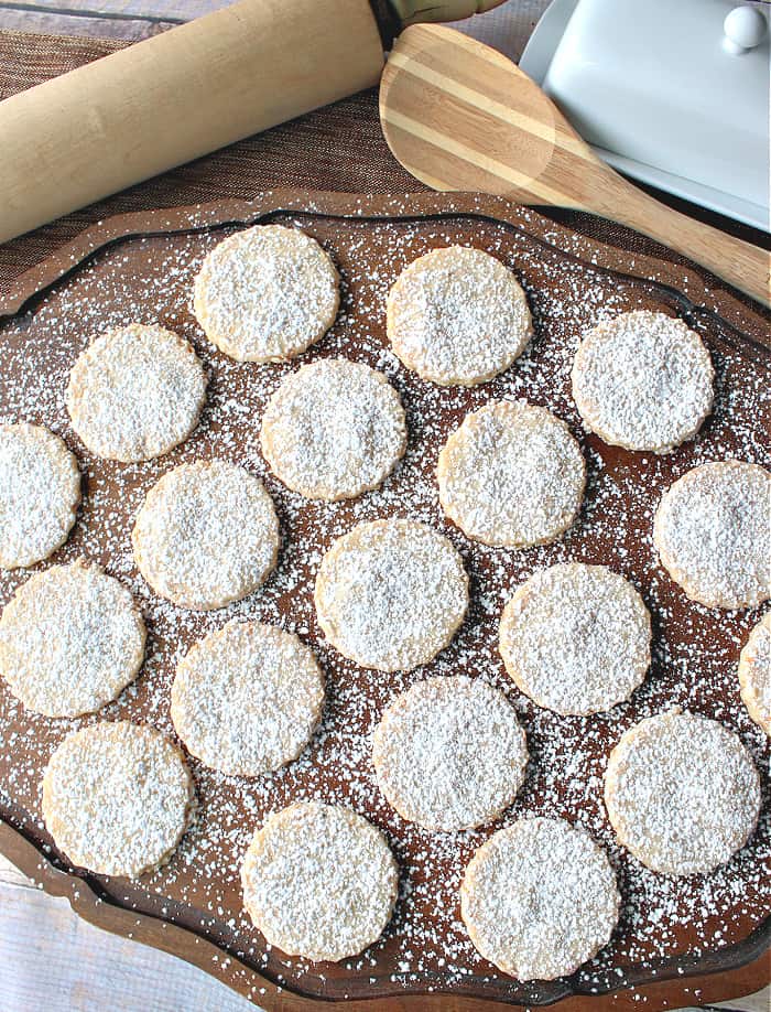 An overhead vertical image of a bunch of round Toasted Coconut Shortbread cookies on a wooden platter with confectioners sugar dusting.