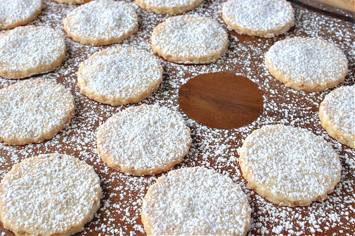 A wooden tray filled with confectioners sugar dusted Shortbread Cookies with one cookie missing.
