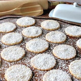 A wooden platter filled with Toasted Coconut Shortbread Cookies dusted with confectioners sugar.