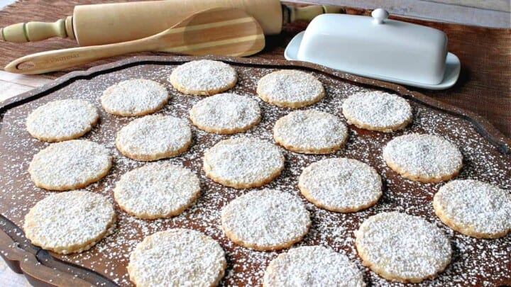 A wooden platter filled with Toasted Coconut Shortbread Cookies dusted with confectioners sugar.