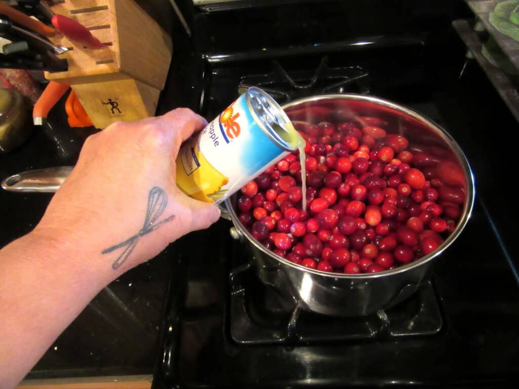 Pineapple juice being added to a saucepan of cranberries.