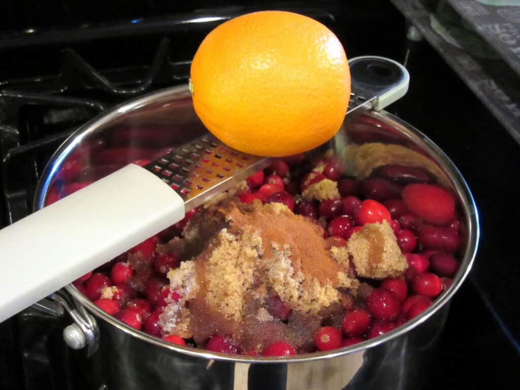 An orange being zested into a pan of cranberries for sauce.