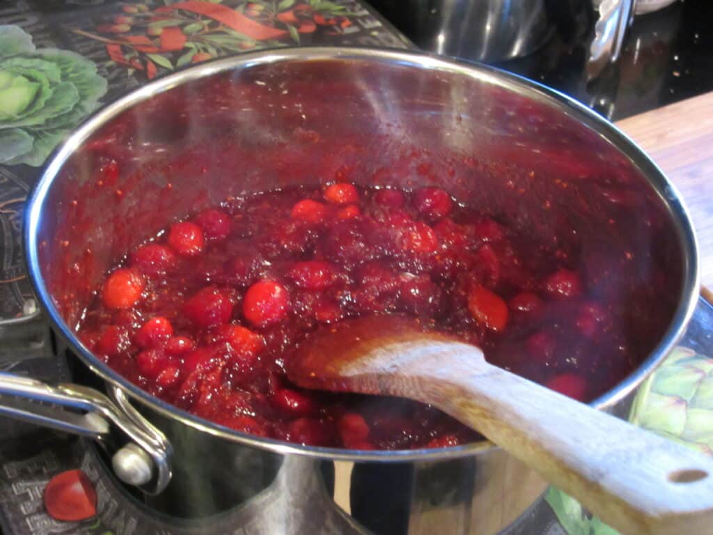 A wooden spoon in a saucepan of whole berry cranberry sauce.