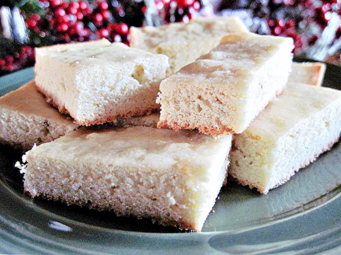 A closeup vertical photo of sliced Anise Cookies on a green plate with red berries in the background.