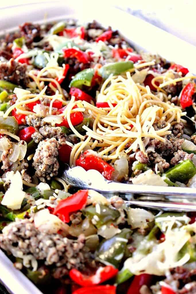An extreme closeup of Christmas Pasta with tongs, sausage, onions, red and green peppers.