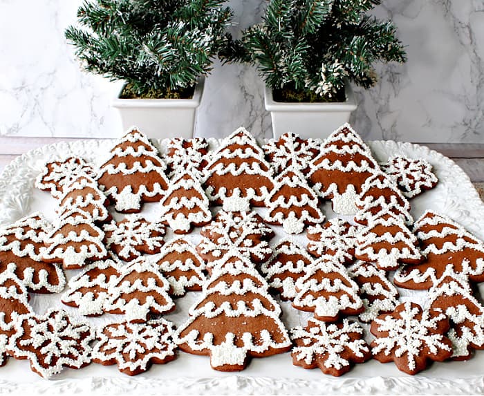 A horizontal photo of a white platter filled with pretty brown and white Gingerbread Trees and Snowflake Cookies for Christmas.