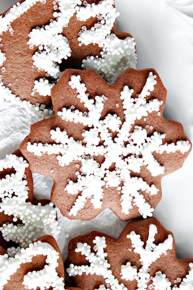 A super closeup vertical photo of a Gingerbread Snowflake Cookie with royal icing, white nonpareils, and white sanding sugar.