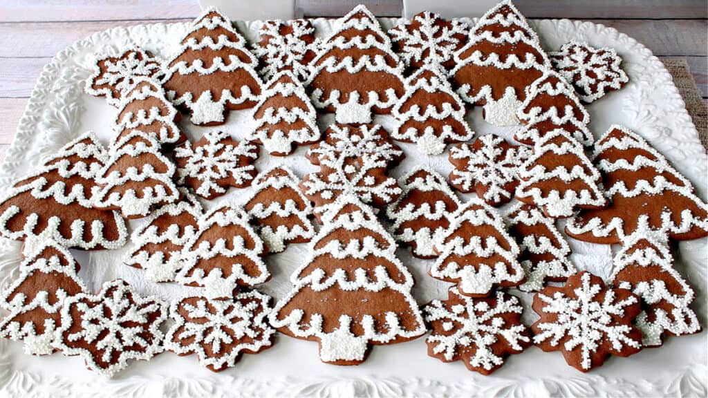 A large white platter filled with iced Gingerbread Trees and Snowflake Cookies with nonpareils and royal icing.