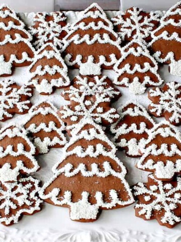 A large white platter filled with iced Gingerbread Trees and Snowflake Cookies with nonpareils and royal icing.