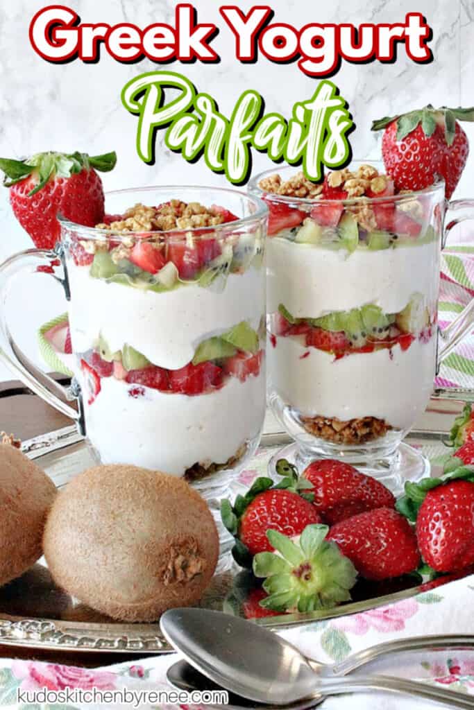 A vertical closeup image of two pretty Greek Yogurt Parfaits on a silver tray garnished with fresh strawberries and a title text overlay graphic.