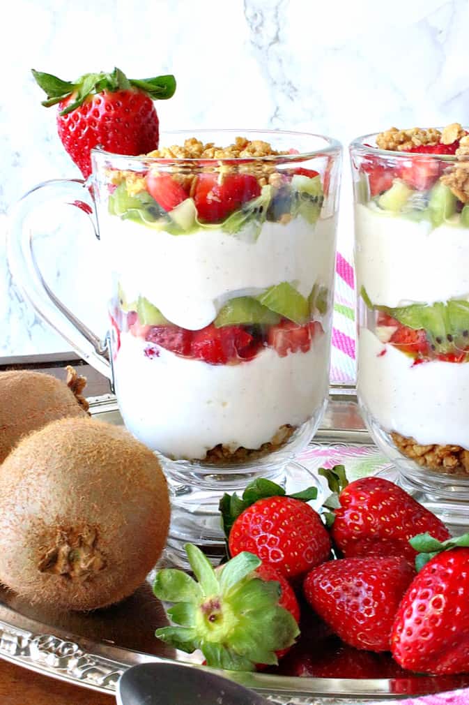 A closeup vertical image of a Greek Yogurt Parfait layered with kiwi, strawberry, and granola in a glass Irish coffee mug.